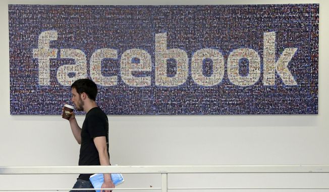 In this March 15, 2013, file photo, a Facebook employee walks past a sign at Facebook headquarters in Menlo Park, Calif. (AP Photo/Jeff Chiu, File)