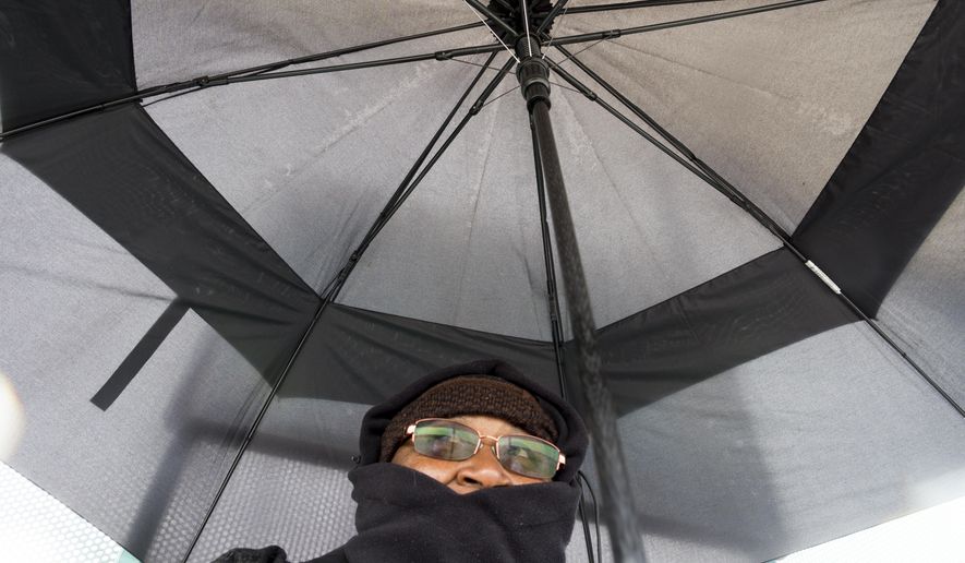 Janet waits for her bus under the cover of a new umbrella at a bus stop in Adelanto, Calif., as rain began to fall on Wednesday, March 21, 2018. (James Quigg/The Daily Press via AP)