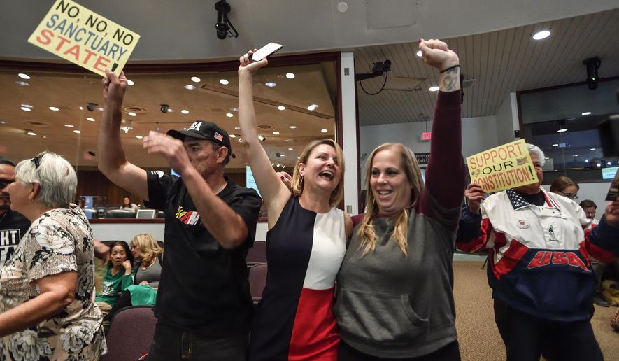 David Hernandez, left, Genevieve Peters, center, and Jennifer Martinez celebrate after the Orange County Board of Supervisors voted to join the U.S. Department of Justice lawsuit against the State of California's sanctuary cities law (SB54) during their meeting in Santa Ana, Calif., Tuesday, March 27, 2018. (Jeff Gritchen/The Orange County Register via AP)