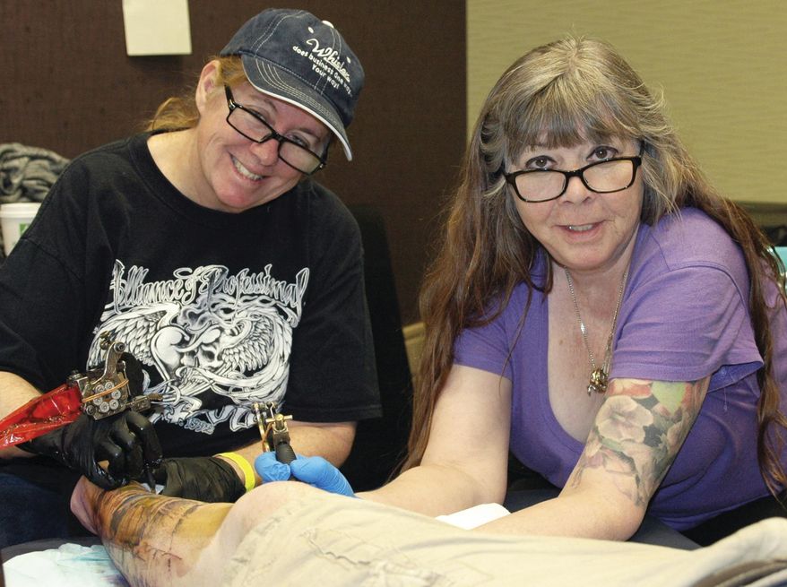 In this March 23, 2018 photo, tattoo artists Judy Parker, left and Sharon Brouse work on a tattoo at Inkfest 2018 Tattoo and Arts Convention in Rock Springs, Wyo. Parker and Brouse are not only connected through their friendship. They also have one very important thing in common: they together have paved the way for women in the tattoo industry. (Ann Jantz/Daily Rocket-Miner via AP)