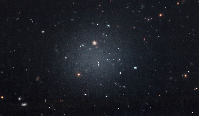 This Nov. 16, 2017 image made with the Hubble Space Telescope shows the diffuse galaxy NGC 1052-DF2, lighter area in center. Several other galaxies can be seen through it. The unusual galaxy’s stars are speeding around with no apparent influence from dark matter, according to a study published on Wednesday, March 28, 2018 in the journal Nature. (P van Dokkum/NASA/ESA via AP)