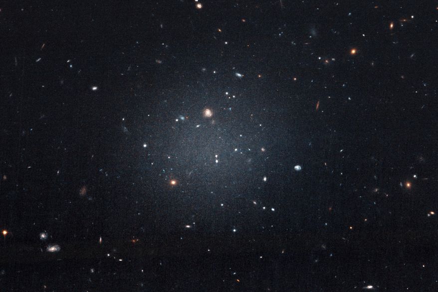 This Nov. 16, 2017 image made with the Hubble Space Telescope shows the diffuse galaxy NGC 1052-DF2, lighter area in center. Several other galaxies can be seen through it. The unusual galaxy’s stars are speeding around with no apparent influence from dark matter, according to a study published on Wednesday, March 28, 2018 in the journal Nature. (P van Dokkum/NASA/ESA via AP)