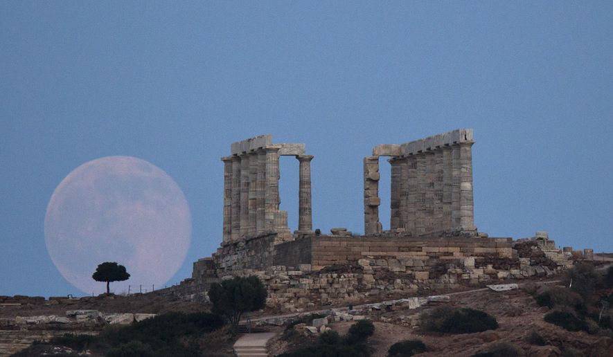 FILE - In this June 20, 2016 file photo, the full moon rises near the ancient marble Temple of Poseidon at Cape Sounion, southeast of Athens. The Greek government has slammed a decision by the country’s powerful archaeological council not to allow the BBC to film part of a serialized adaptation of a John le Carre novel in Cape Sounion, site of an ancient temple of Poseidon. Lefteris Kretsos, general secretary for media and communication, said on Thursday, March 29, 2018 the decision by the Central Archaeological Council, or KAS, to reject the BBC’s request to film part of The Little Drummer Girl in Sounion “highlights once again the issues we have as a country.” (AP Photo/Petros Giannakouris, file)