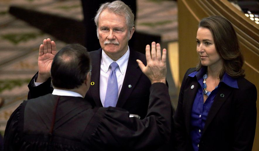 FILE - In this Jan. 12, 2015, file photo, Oregon Gov. John Kitzhaber, left, is joined by his fiancee, Cylvia Hayes, as he is sworn in for an unprecedented fourth term in Salem, Ore. The Oregon Government Ethics Commission has voted to accept a settlement with former Gov. Kitzhaber that requires him to pay a $20,000 fine for violating state ethics laws. Kitzhaber attended a meeting Friday, March 30, 2018, in Salem and expressed regret for his mistakes, The Statesman Journal reported. (AP Photo/Don Ryan, File)