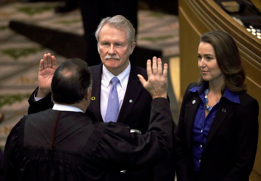 FILE - In this Jan. 12, 2015, file photo, Oregon Gov. John Kitzhaber, left, is joined by his fiancee, Cylvia Hayes, as he is sworn in for an unprecedented fourth term in Salem, Ore. The Oregon Government Ethics Commission has voted to accept a settlement with former Gov. Kitzhaber that requires him to pay a $20,000 fine for violating state ethics laws. Kitzhaber attended a meeting Friday, March 30, 2018, in Salem and expressed regret for his mistakes, The Statesman Journal reported. (AP Photo/Don Ryan, File)