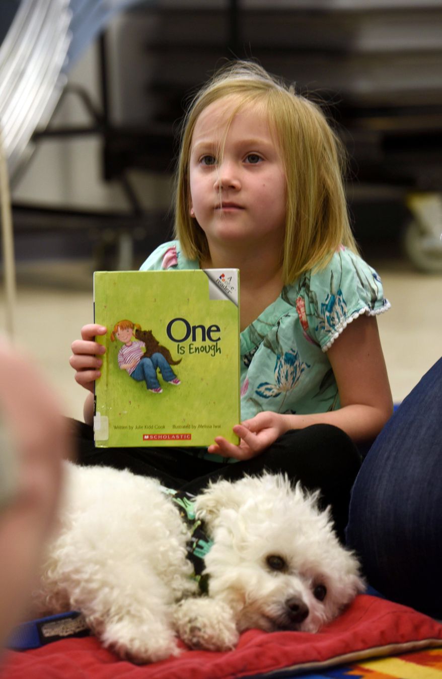 This March 17, 2018 photo shows Gracie Kennedy, 6, holding a book she read to Buster during the Pet Partners Read With Me program at the Tryon Branch Library in Pensacola, Fla. The program is a special initiative to promote literacy and instill a lifelong love of reading by having children read to therapy animals.(John Blackie/Pensacola News Journal via AP)