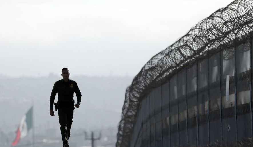 In this June 22, 2016, file photo, Border Patrol agent Eduardo Olmos walks near the secondary fence separating Tijuana, Mexico, background, and San Diego in San Diego. (AP Photo/Gregory Bull, File)