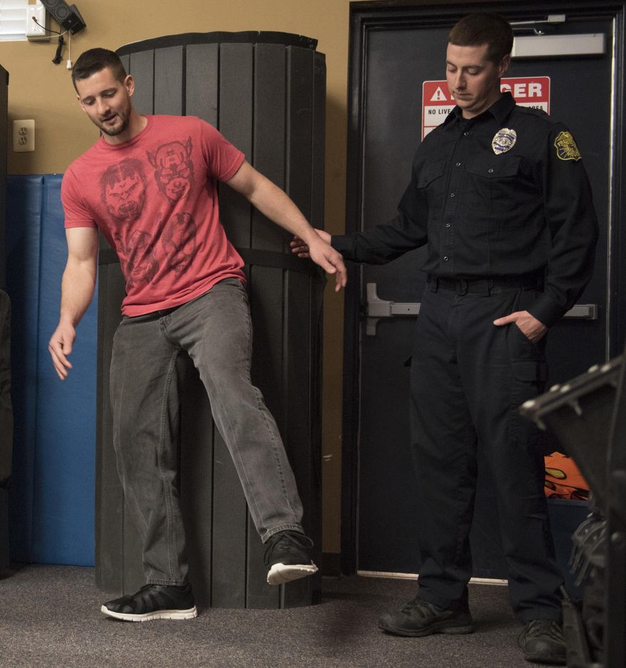 In this March 2018 photo, volunteer Paul Foelber loses his balance as Officer 1st Class Sean Geiser stands watch in case he falls during a sobriety test performed by recruits during a DUI enforcement training session in Frederick, Md. Recruits get hands-on DUI enforcement training thanks to tipsy volunteers. (Graham Cullen/The Frederick News-Post via AP)