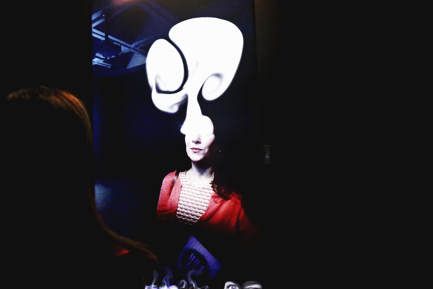 An attendee at North Carolina Museum of Art's "You Are Here: Light, Color, and Sound Experiences " media preview interacts with Rafael Lozano-Hemmer's "The Year's Midnight (Shadow Box #5)" on April 4, 2018 in Raleigh, N.C.  Billed as "more than an exhibition, an experience," the show stretches throughout the museum's East Building and even the outdoor park. It consists of immersive and interactive installations by 14 contemporary artists, including Kusama and Cardiff. (Juli Leonard /The News & Observer via AP)