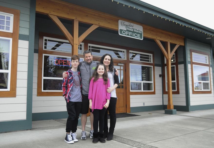 In this March 30, 2018, photo, Jason Doig, his wife Jeni and children Ethan 10, and Rylie, 10, stand outside Doig's business, Bliemeisters' Wood Works in Carlsborg, Wash. Doig was awarded the Carnegie Medal for heroism after risking his life preventing a woman from jumping off the Hood Canal Bridge in March 2017. (Jesse Major/The Peninsula Daily News via AP)