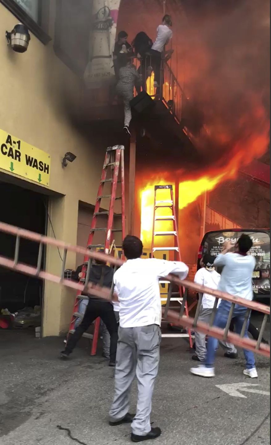 In this Monday, April 9, 2018 photo, girls flee a second-story dance studio onto a balcony as a roaring fire engulfs their building in Edgewater, N.J. About 15 girls were treated for minor injuries, Mayor Michel Joseph McPartland said. (Ilker Kesiktas via AP)
