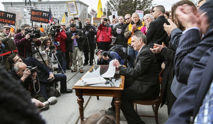 Vermont's Gov. Phil Scott finishes signing the first significant gun restrictions bills in the state's history during a ceremony on the steps of the Statehouse in Montpelier, Vt., Wednesday, April 11, 2018. (AP Photo/Cheryl Senter)