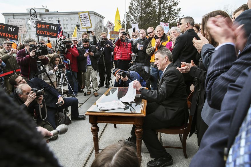 Vermont's Gov. Phil Scott finishes signing the first significant gun restrictions bills in the state's history during a ceremony on the steps of the Statehouse in Montpelier, Vt., Wednesday, April 11, 2018. (AP Photo/Cheryl Senter)