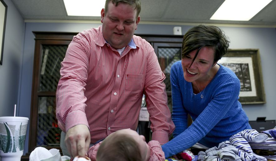 In this March 23, 2018 photo, Philip Ellison and his wife, Katherine Ellison, change their son Patton's clothing at the end of the work day at Philip Ellison's firm Outside Legal Counsel in Hemlock, Mich. If you were born in Michigan in July 1984 or later, you may be among more than five million people whose blood is being held by the state of Michigan, some of which may be used in medical research. A federal lawsuit, filed by Saginaw County Attorney Ellison on behalf of a group of Michigan parents, argues that the practice is unconstitutional and there are no protections in place to stop police or others from accessing the information that can be derived from stored blood samples. (Henry Taylor/The Flint Journal-MLive.com via AP)