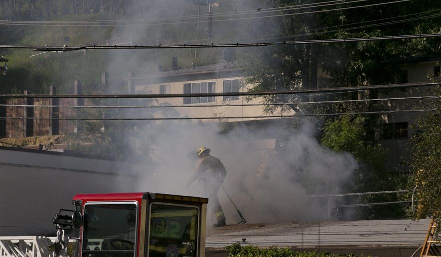 A Los Angeles firefigher is surrounded by heavy smoke as he knocks down hot spots on the roof of a music studio in Los Angeles Saturday, April 14, 2018. Officials says two people were killed and at least three others were hurt when flames ripped through the studio. (AP Photo/Damian Dovarganes)