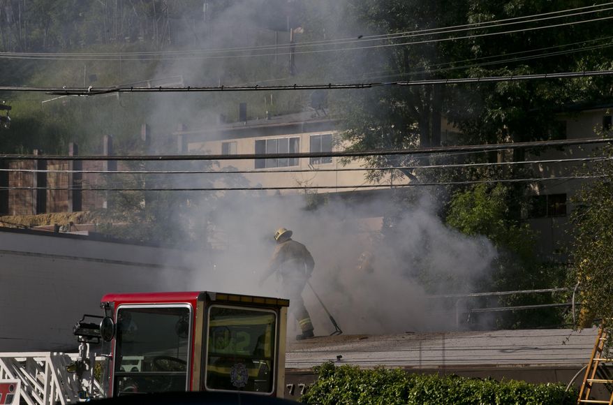 A Los Angeles firefigher is surrounded by heavy smoke as he knocks down hot spots on the roof of a music studio in Los Angeles Saturday, April 14, 2018. Officials says two people were killed and at least three others were hurt when flames ripped through the studio. (AP Photo/Damian Dovarganes)