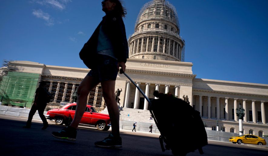 FILE - In this Jan. 18, 2018 file photo, a tourist walks with her suitcase in front of the Capitolio in Havana, Cuba. President Donald Trump drew cheers from a Cuban-American crowd last summer when he announced that he was rolling back some of Barack Obama&#x27;s opening to Cuba in order to starve the island&#x27;s military-run economy of U.S. tourism dollars and ratchet up pressure for regime change. (AP Photo/Ramon Espinosa, File)