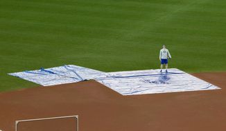 Toronto Blue Jays coach Tim Leiper looks up from tarps protecting the field at Rogers Centre from water coming through the roof in Toronto on Monday April 16, 2018. The Blue Jays baseball game against the Kansas City Royals was cancelled over safety concerns when ice falling from the CN Tower punched a hole in the roof. (Fred Thornhill/The Canadian Press via AP)