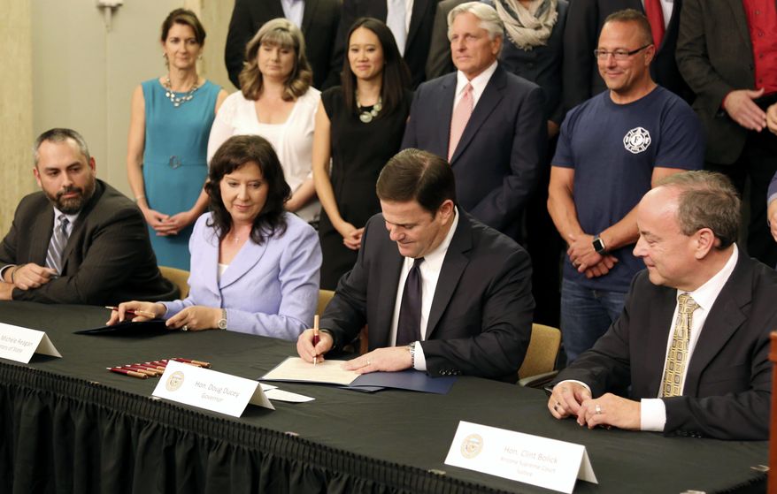FILE- In this May 26, 2016, file photo, Arizona Gov. Doug Ducey, second from right, signs a proclamation certifying the results of Proposition 123 on school funding at the state Capitol in Phoenix. A Phoenix man who won a federal court ruling finding Arizona distributed more than $344 million to schools since 2016 without Congressional approval won't ask for the money to be repaid because Congress finally approved the payouts last month. (AP Photo/Ryan Van Velzer, File)