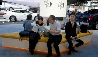 FILE - In this April 19, 2017, file photo, visitors to the stands of GM brands Chevrolet and Buick seat near a section promoting electric power during Auto Shanghai 2017 show at the National Exhibition and Convention Center in Shanghai, China. China has announced plans to allow full foreign ownership of automakers in five years, ending restrictions that have strained relations with Washington and other trading partners. (AP Photo/Ng Han Guan, File)