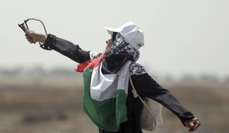 A Palestinian woman hurls stones at Israeli troops during a protest at the Gaza Strip&#x27;s border with Israel, Friday, April 20, 2018. Since weekly mass marches began in late March, 28 Palestinians have been killed and hundreds wounded by Israeli army fire from across the border fence.(AP Photo/ Khalil Hamra)