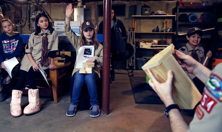 In a Thursday, March 1, 2018 photo, Tatum Weir, center, raises her hand as she prepares to ask a question while going over plans to build a tool box during a cub scout meeting in Madbury, N.H. Fifteen communities in New Hampshire are part of an "early adopter" program to allow girls to become Cub Scouts and eventually Boy Scouts. Tatum and her twin brother Ian are planning to become the first set of girl-boy siblings to become Eagle Scouts. (AP Photo/Charles Krupa)