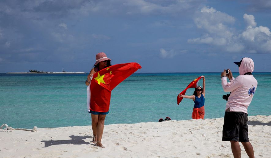 In this Sept. 14, 2014, file photo, Chinese tourists take souvenir photos with a Chinese national flag as they visit Quanfu Island, one of Paracel Islands of Sansha prefecture of southern China's Hainan province in the South China Sea. (AP Photo/Peng Peng, File)