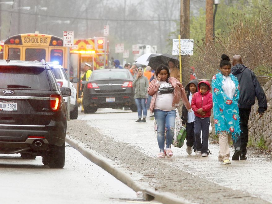 A family walks away from the scene after a school bus was involved in a multi-vehicle crash Monday, April 23, 2018, in Cincinnati. (Cameron Knight/The Cincinnati Enquirer via AP)