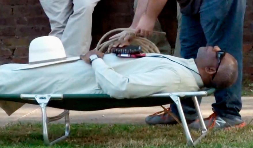 FILE - In this Tuesday, April 17, 2018, file image from video provided by KTHV-TV, a death penalty protester outside the Arkansas governor's mansion in Little Rock prepares to tie rope around Pulaski County Circuit Judge Wendell Griffen. The protesters were marking one year since Arkansas conducted a series of executions. Arkansas Supreme Court justices on Tuesday, April 24, 2018, appealed a ruling that allows Griffen to move forward with a lawsuit challenging his disqualification from execution cases following his participation in an anti-death penalty demonstration. (KTHV/TEGNA Inc. via AP, File)