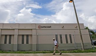 FILE- In this Oct. 12, 2017, file photo a pedestrian walks by a Comcast Service Center, in Miami. Comcast Corp. reports earnings Wednesday, April 25, 2018. (AP Photo/Alan Diaz, File)