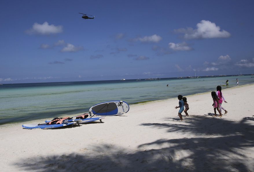 Children watch as a military helicopter passes by the country's most famous beach resort island of Boracay, in central Aklan province, Philippines Wednesday, April 25, 2018, a day before the government implements its temporary closure. Thousands of workers will be affected when Boracay will be closed after Philippine President Rodrigo Duterte orders its closure on April 26 for up to six months after saying the waters off its famed white-sand beaches had become a "cesspool" due to overcrowding and development. (AP Photo/Aaron Favila)