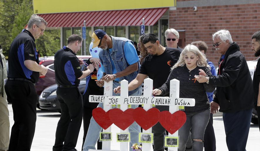 Family members of people killed at a Waffle House restaurant write messages on wooden crosses set up as a memorial Wednesday, April 25, 2018, in Nashville, Tenn. Four people were killed when a gunman opened fire at the restaurant Sunday. Members of the Waffle House management and staff joined the family members as the restaurant re-opened Wednesday. (AP Photo/Mark Humphrey)
