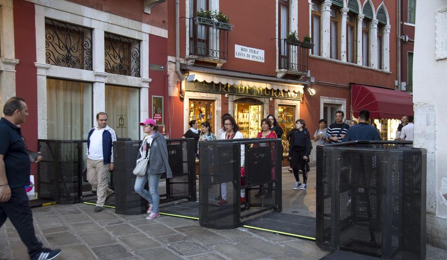 In this photo taken on Friday, April 27, 2018, people walk through gates in Venice, Italy. Venice has resorted to installing gates at the ends of two bridges to turn back tourists if their numbers become overwhelming. The temporary measure was put in place Saturday in the lagoon city for a four-day holiday weekend culminating on Labor Day, May 1. (Riccardo Gregolin/ANSA via AP)