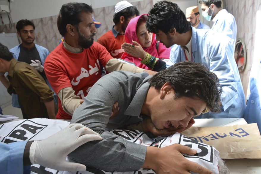 A Pakistani volunteer comforts a grief-stricken person from Shiite community, mourns over a body of his family member at a mortuary in Quetta, Pakistan, Saturday, April 28, 2018. Gunmen attacked an electronics shop and fatally shot two shopkeepers, both of them minority Hazara Shiites, said Mohammad Alam, area police officer. (AP Photo/Arshad Butt)