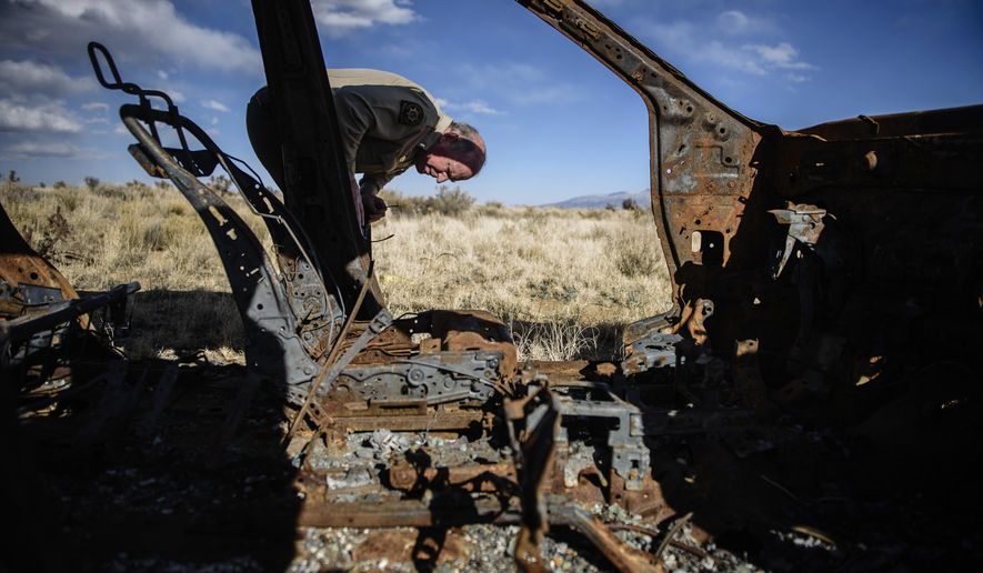 In this Feb. 23, 2018 photo, Lt. Keith Elder, of the Sandoval County Sheriff's Office, examines the rusted and burned out hull of a Nissan left on the side of a dirt road in the Rio Rancho Estates area west of the city in Nev. (Roberto E. Rosales/The Albuquerque Journal via AP)