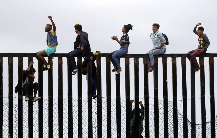 Central American migrants sit on top of the border wall on the beach in San Diego during a gathering of migrants living on both sides of the border, Sunday, April 29, 2018. (AP Photo/Chris Carlson)