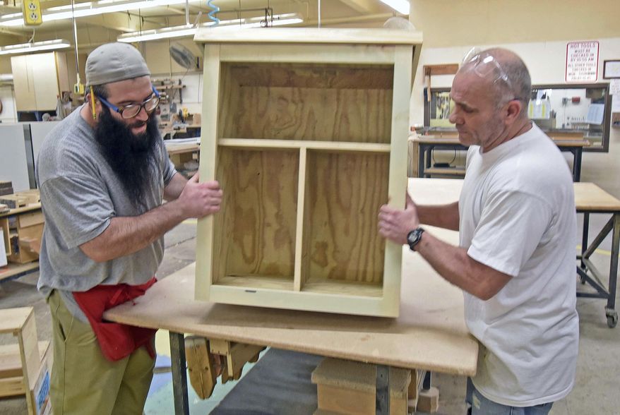 In this April 24, 2018 photo, Nick Webster, left, and Brian Reddig show off a Little Free Pantry's in the workroom of Rough Rider Industries in Bismarck, N.D. Webster said he and Reddig are making 16 of the pantry boxes with each taking a half-hour to 45 minutes to complete. A community effort to fight hunger in the Bismarck-Mandan area is expanding. The Little Free Pantries effort involves business-sponsored wooden boxes stocked with food and personal care items. (Tom Stromme/The Bismarck Tribune via AP)
