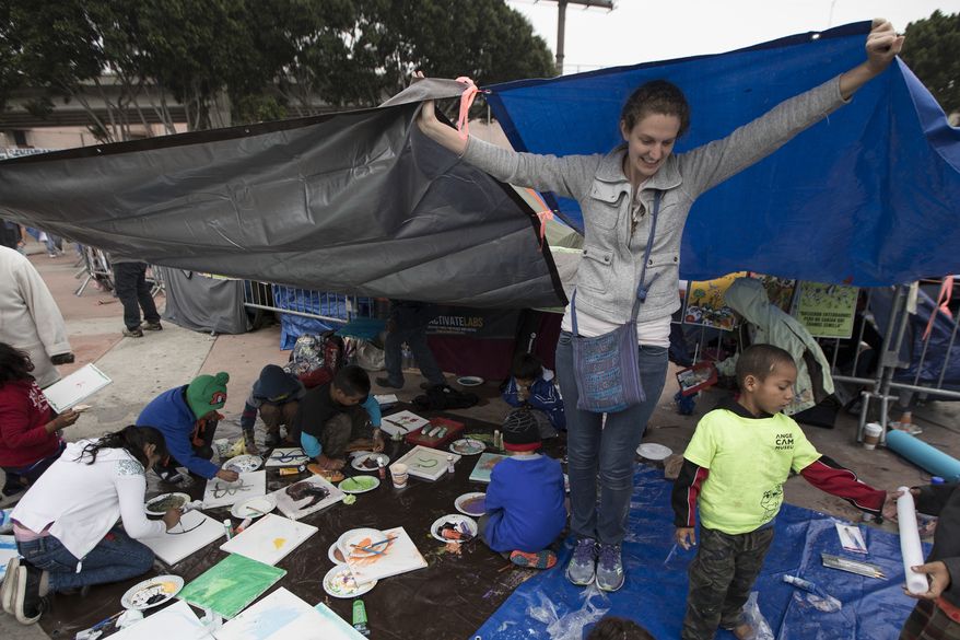A volunteer holds up tarps to protect children from the rain at the El Chaparral U.S.-Mexico border crossing, in Tijuana, Mexico, Wednesday, May 2, 2018, where the caravan of Central Americans seeking asylum in the United States have set up camp. Some migrants in the caravan of have started what will likely be a long process. About 28 were accepted for processing Monday and Tuesday by U.S. border inspectors at a San Diego crossing. (AP Photo/Hans-Maximo Musielik)