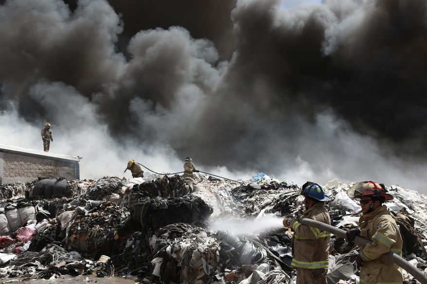 Firefighters try to extinguish a fire at a recycling plant on the outskirts of Ciudad Juarez, Mexico, Wednesday, May 2, 2018. Juarez authorities declared an environmental emergency due to harmful particulate matter in the smoke, and people in its path were advised to stay inside, shut windows and doors and not use air conditioners under any circumstances. (AP Photo/Christian Torres)