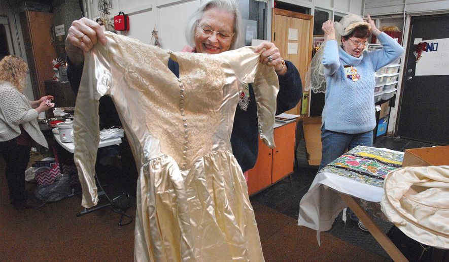 In this April 16, 2018 photo, Leslie Frizzell left, and Kay Brook measure up a wedding dress  that was donated to Fibers of Love in Bloomington, Ill. The dress will be cut up and made into burial gowns for stillborn infants by the group.About 50 women in the Fibers of Love group come together every Monday from April through December in Bloomington to spend the day creating items for social service agencies in Central Illinois and around the world. the group have used their talent to touch thousands of lives over 25 years with gifts of dignity, warmth and comfort. (David Proeber/The Pantagraph via AP)