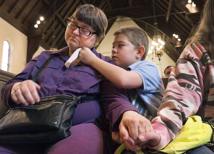 In this April 20, 2018 photo provided by Steve Bohnstedt, Nicholas Weible, offers his mom, Wendy Smith a tissue during the memorial service for his father, Christopher Weible, held at First Christian Church in Quincy, Ill. Adams County Coroner James Keller is facing sharp criticism for how he handles poor people who can't afford to bury their loved ones: He has them sign over their rights to the deceased, leaving them without the death certificate, then cremates the body and keeps the ashes until the family pays $1,000. After Weible died last month, his family held a memorial service with just a photograph and an empty container. Weible and his ex-wife, Wendy were both on disability and she didn't have $1,000 to get his ashes. (Steve Bohnstedt via AP)
