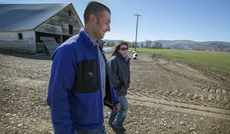 In this March 20, 2018 photo, farmer Jackie Brunson, right, walks with Tuusso Energy co-founder Jason Evans, whose project would place photovoltaic panels on some of the Brunson land and property belonging to three other Kittitas County landowners, in Ellensburg, Wash. (Steve Ringman /The Seattle Times via AP)