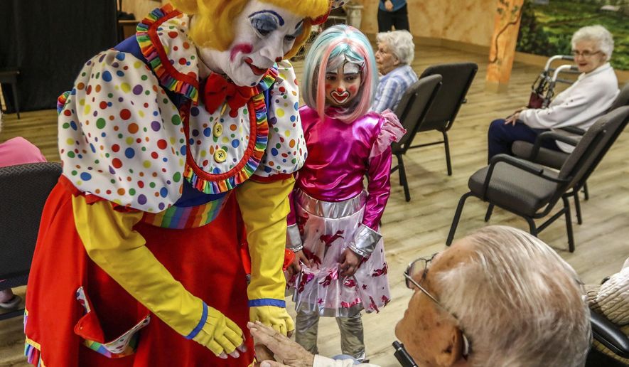 In this Saturday, April 28, 2018 photo, Cupcake T. Clown, and Starfire aka Addie Brisbois greet a resident of Riverview Terrace, a residential living facility for seniors, before a show presented by the Eastwood Clown College in Roseburg, Ore. For the past four years, the program has taught students from Eastwood Elementary School in Roseburg how to be clowns. (Mike Henneke/The News-Review via AP)