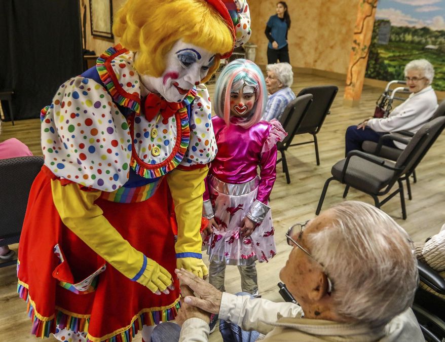 In this Saturday, April 28, 2018 photo, Cupcake T. Clown, and Starfire aka Addie Brisbois greet a resident of Riverview Terrace, a residential living facility for seniors, before a show presented by the Eastwood Clown College in Roseburg, Ore. For the past four years, the program has taught students from Eastwood Elementary School in Roseburg how to be clowns. (Mike Henneke/The News-Review via AP)