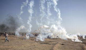 Palestinian protesters run for cover from teargas fired by Israeli troops during a protest at the Gaza Strip&#x27;s border with Israel, Tuesday, May 15, 2018. Israel faced a growing backlash Tuesday and new charges of using excessive force, a day after Israeli troops firing from across a border fence killed dozens of Palestinians and wounded more than 2,700 at a mass protest in Gaza. (AP Photo/Khalil Hamra)
