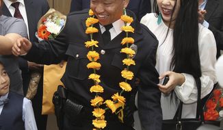 In this photo taken May 4, 2018, Damber D. Subba, center, of Akron, stands next to his wife Tara Subba as he is showered with flowers, a cultural Bhutanese tradition of celebrating a success, from his family after being sworn in as the first Bhutanese refugee in the Akron Police Department during a ceremony at the Akron-Summit County Public Library in Akron, Ohio. (Karen Schiely/Akron Beacon Journal via AP)