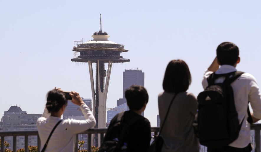 Tourists look across at the Space Needle, where a floor of scaffolding remains below the upper portion, in Seattle on Tuesday, May 22, 2018. The family-owned landmark is set to unveil the biggest renovation in its 56-year history next month, a $100 million investment in a single year of construction that transformed the structure&#x27;s top viewing level some 500-feet above ground. (AP Photo/Elaine Thompson)