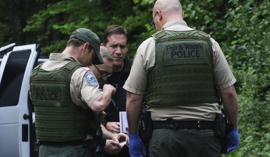 File - In this Saturday, May 19, 2018 file photo, Washington State Fish and Wildlife Police confer with an individual from the King County Medical Examiner's and a King County Sheriff's deputy on a remote gravel road above Snoqualmie, following a fatal cougar attack. Recordings of emergency calls about a fatal cougar attack in Washington state Saturday detail how a dispatcher calmly struggled to figure out where it occurred and how worried the surviving victim was about his friend. Isaac Sederbaum was mountain biking with friend S.J. Brooks on logging roads in the Cascade Mountain foothills east of Seattle when they were attacked. The cougar bit Sederbaum on the head before killing Brooks. (Alan Berner /The Seattle Times via AP, File)