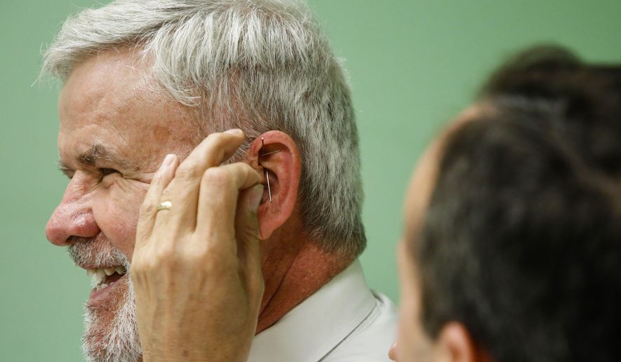 In this photo taken May 9, 2018, Pickaway County Court of Common Pleas Judge P. Randall Knece, laughs as Dr. Kenneth J. Laux, right, places needles in his ear during an acupuncture treatment at Pickaway Area Recovery Services in Circleville, Ohio. With the help of grant money, Dr. Laux began using acupuncture as a way to help treat people recovering from opioid disorder. Judge Knece decided to sit in and receive the treatment in a show of support to the people in recovery at the session. (Joshua A. Bickel/The Columbus Dispatch via AP)