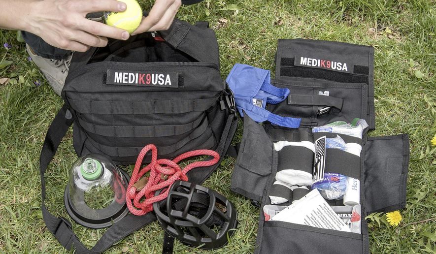 In this May 3, 2018 photo, Paul Fedyniak, who is set to graduate from UI college of veterinary medicine this month, poses with veterinary medical kits he developed for first responders to help police dogs injured in the line of duty in Urbana, Ill. Fedyniak raised donations for the kits he created for K9 units and EMS services after seeing a need for dog-specific medical supplies to help ambulances that could, potentially, transport an injured K9 unit dog to a vet hospital. He also painted dog and cat portraits to raise more money, and he hopes to form a non-profit to continue supplying these kits to police, fire departments and ambulance services after he graduates and goes to work as a veterinarian in Chicago. (Rick Danzl/The News-Gazette via AP )